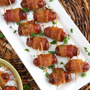 A large batch of bacon wrapped smokies are placed on a white plate.