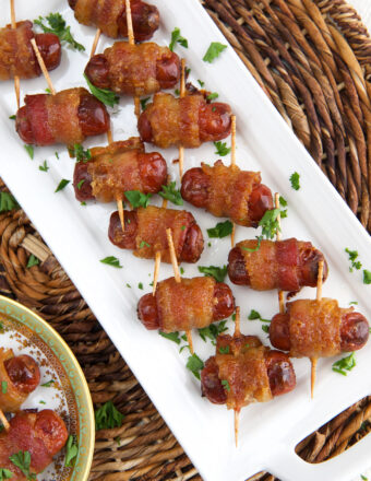 A large batch of bacon wrapped smokies are placed on a white plate.