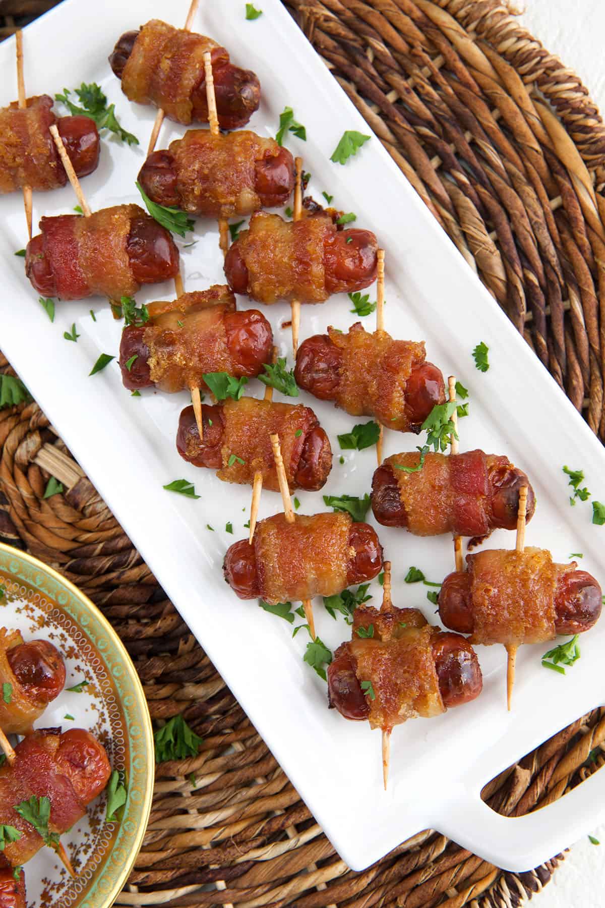 A large batch of bacon wrapped smokies are placed on a white plate. 