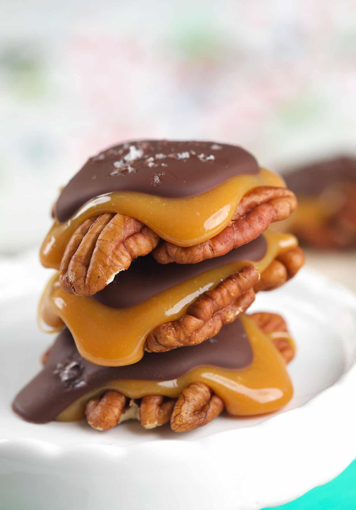 Three chocolate turtles are stacked on a white plate.