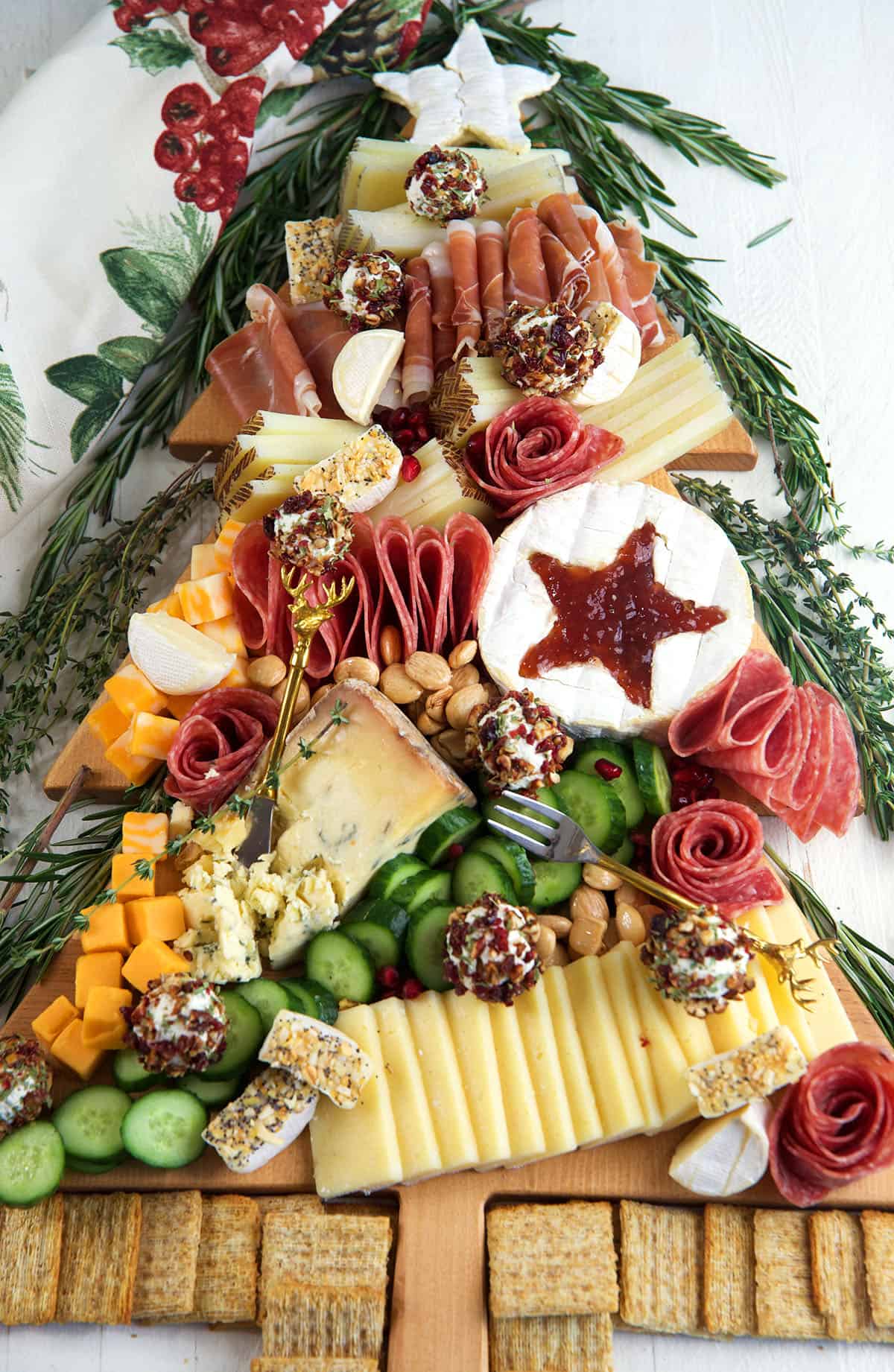 A Christmas tree charcuterie board is surrounded by rosemary and crackers. 