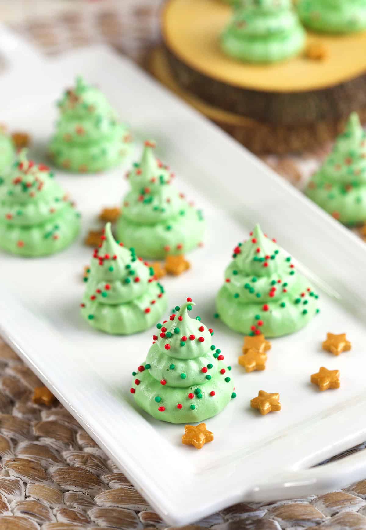 Six tree cookies are placed next to gold stars on a white plate. 
