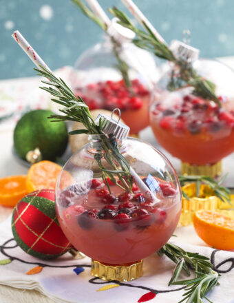 A Christmas ornament cocktail is garnished with rosemary.