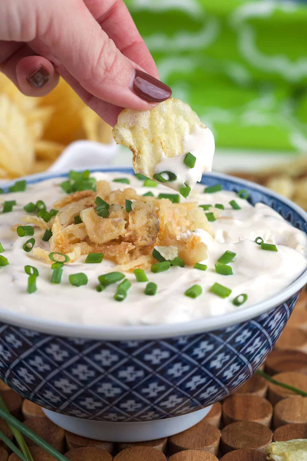 A chip is being dipped into a bowl of french onion dip. 