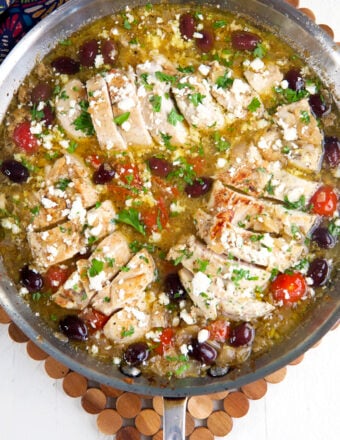 A skillet is filled with greek chicken, feta, tomatoes and olives.
