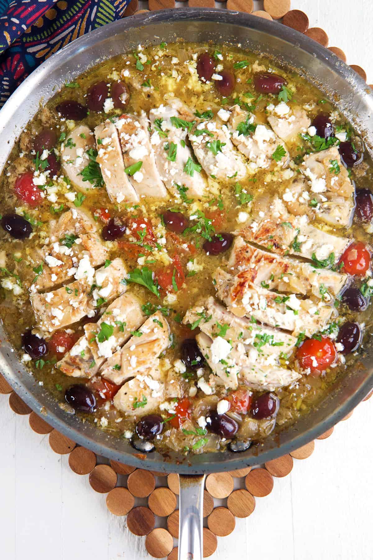 A skillet is filled with greek chicken, feta, tomatoes and olives. 