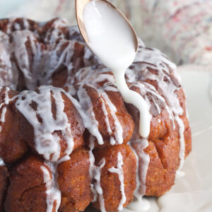 Icing is being drizzled on the monkey bread with a spoon.