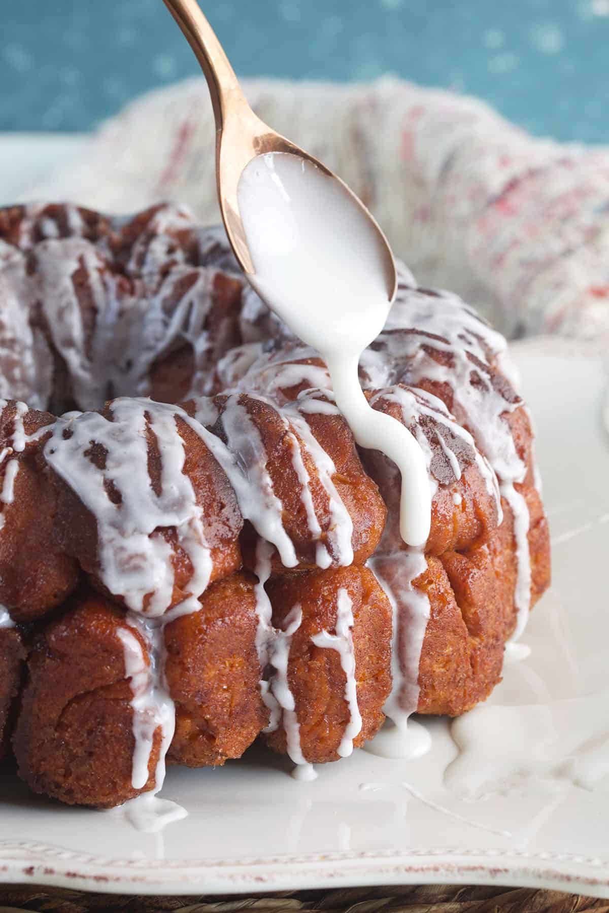 Icing is being drizzled on the monkey bread with a spoon. 