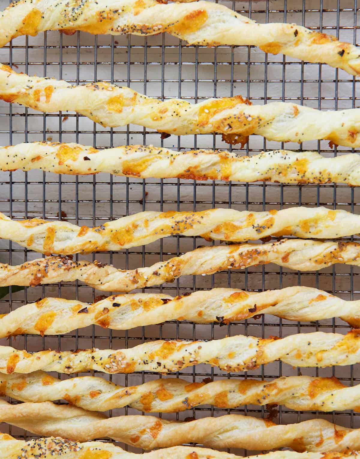 A batch of cheese straws are cooling on a wire rack. 