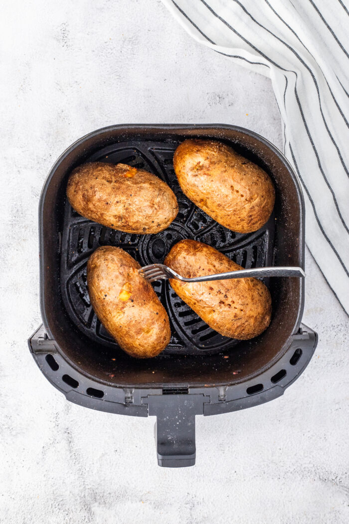 Four cooked potatoes are in an air fryer basket.