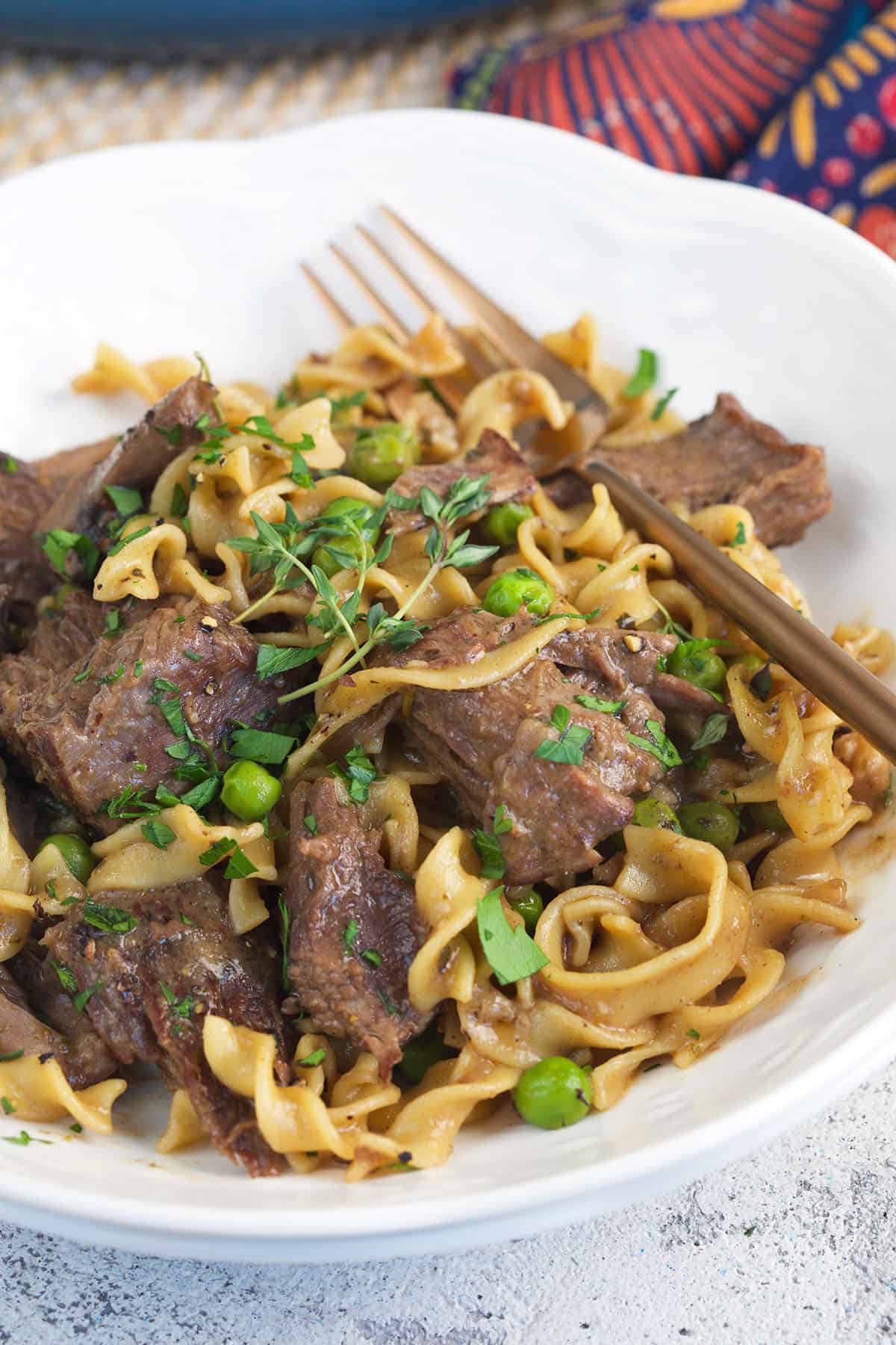 A white plate is topped with beef and noodles. 