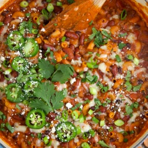 A pot of chili mac is garnished with herbs, jalapenos and cheese.