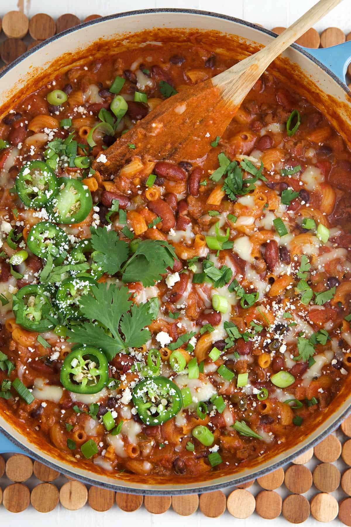 A pot of chili mac is garnished with herbs, jalapenos and cheese. 