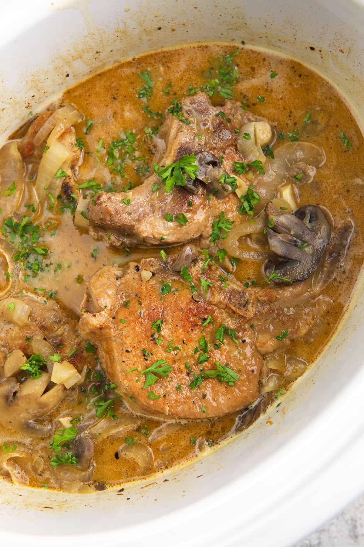 A slow cooker is filled with pork chops, mushrooms and sauce. 