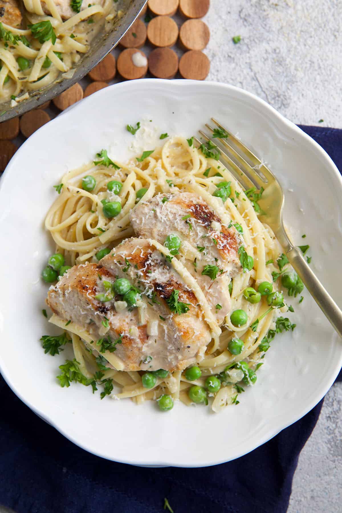 A white plate is topped with a portion of chicken and pasta. 