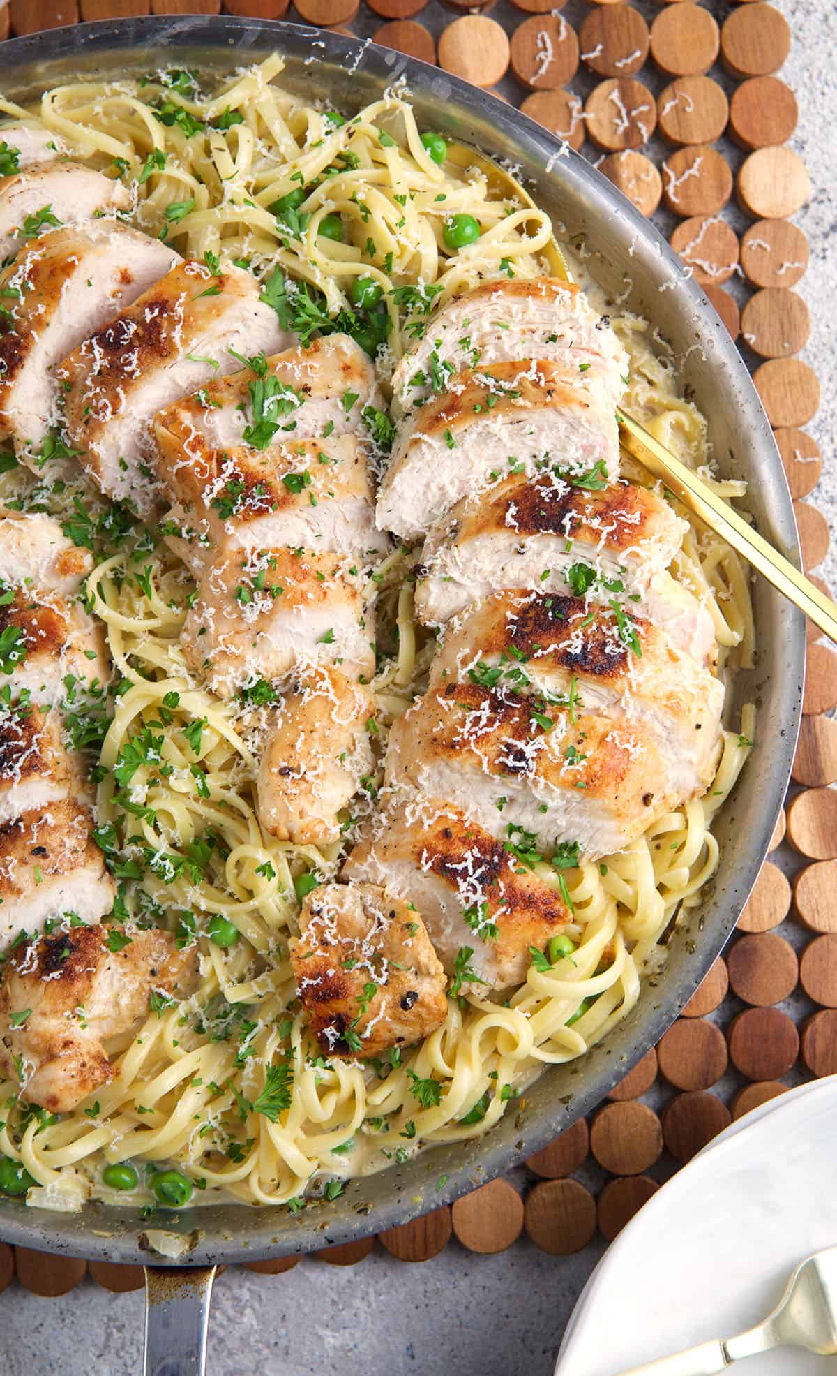 Sliced chicken is placed on top of pasta in a pan. 