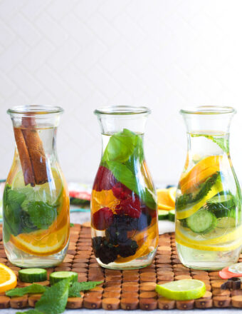 three bottles of infused water with a mix of fruit, vegetables and herbs in them.