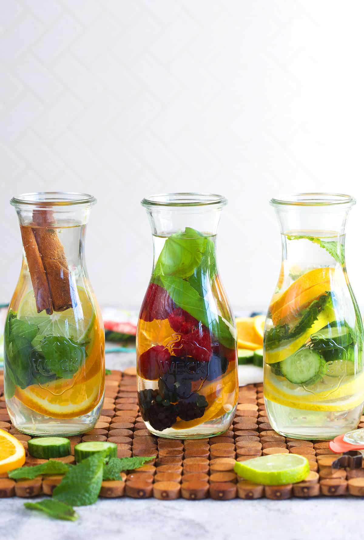 three bottles of infused water with a mix of fruit, vegetables and herbs in them.