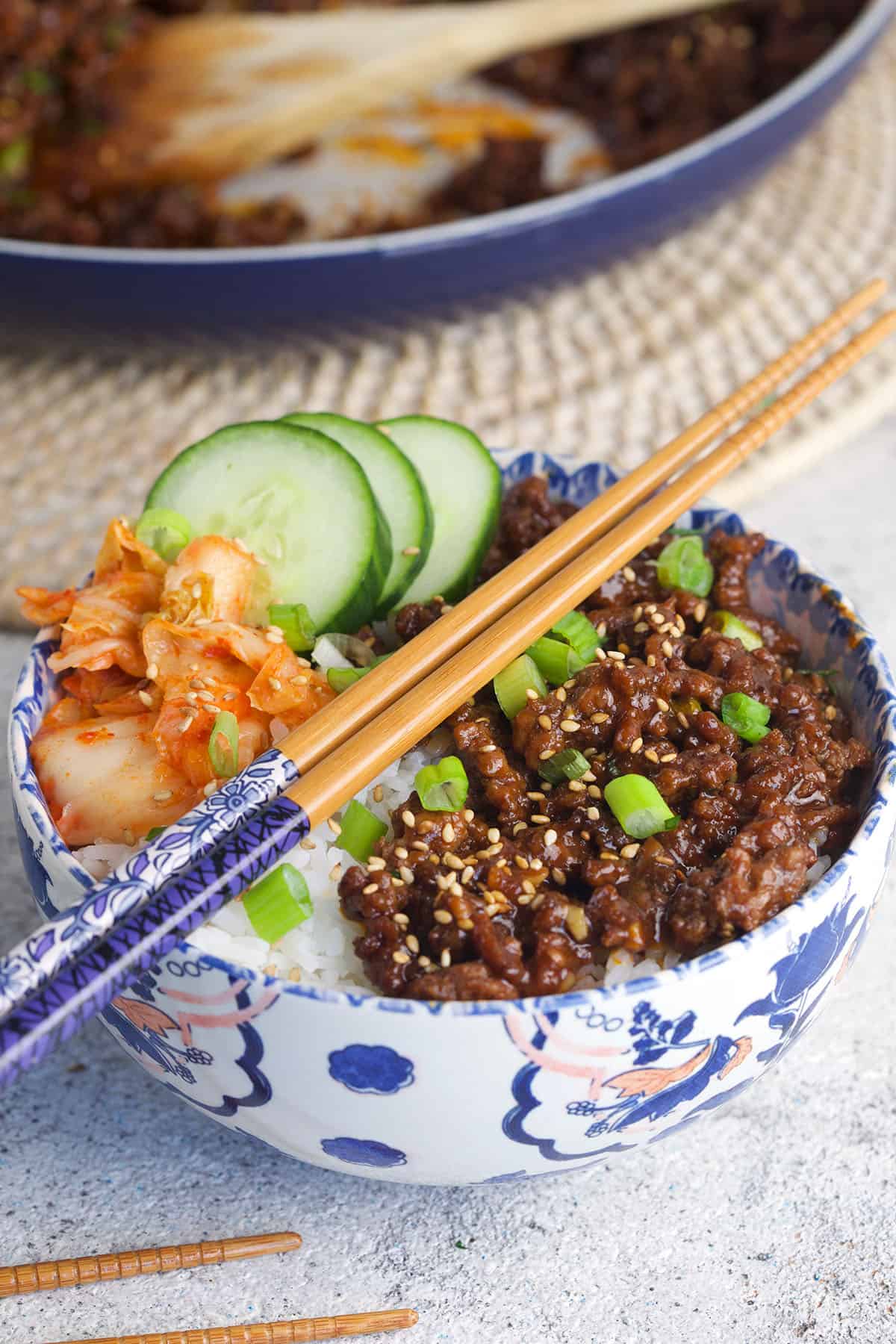 Korean BBQ ground beef is in a bowl with rice, kimchi and cucumbers. 