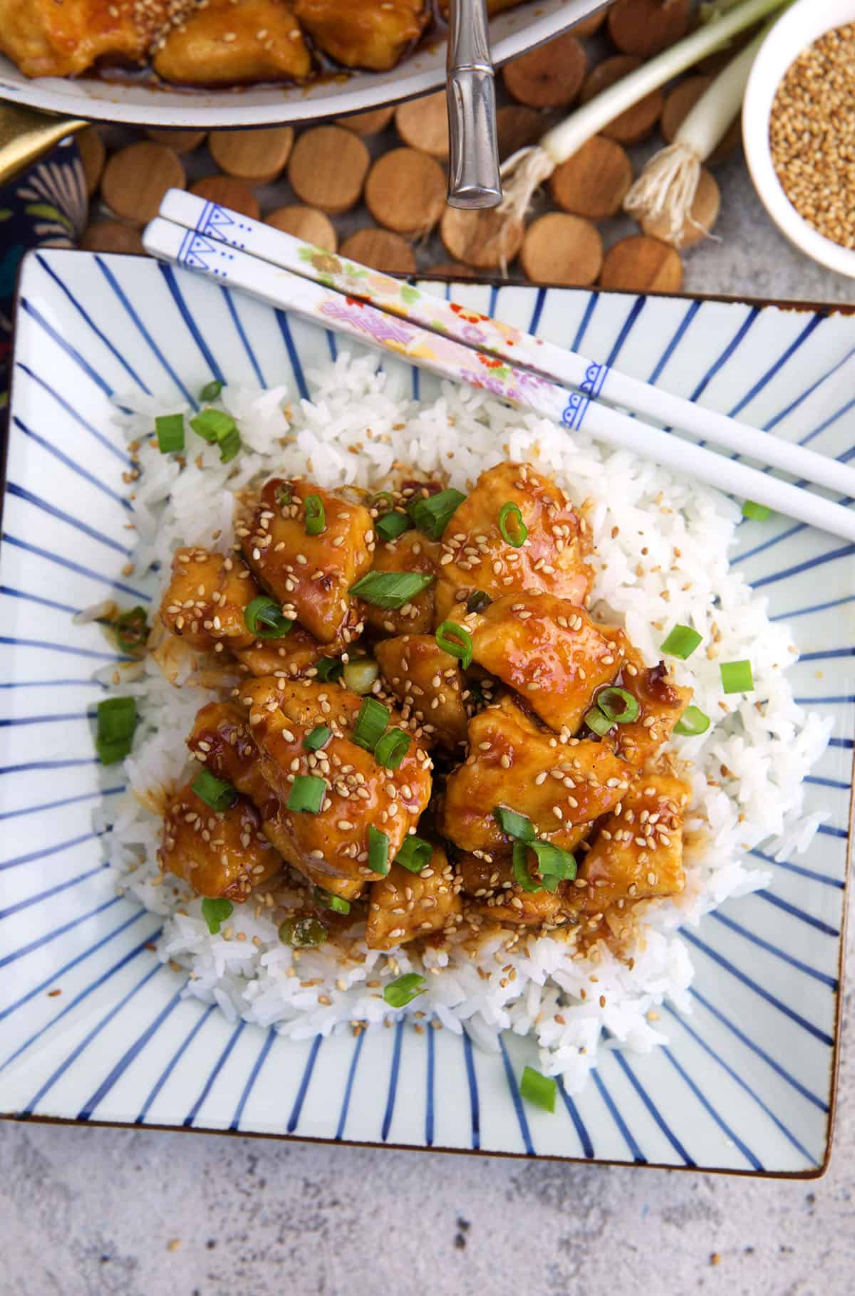 Chopsticks are placed on a plate with rice and sesame chicken. 