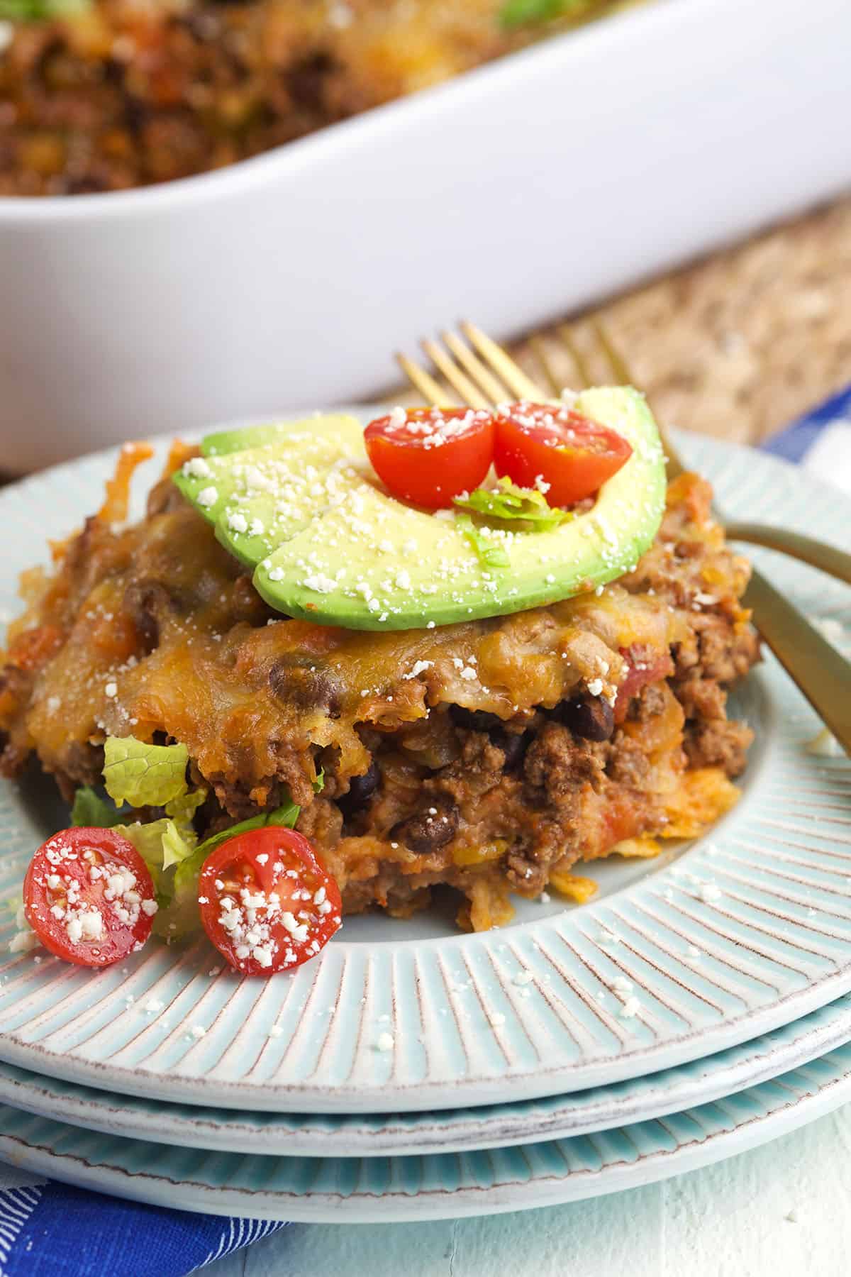 A serving of taco casserole is garnished with tomatoes and avocado slices. 