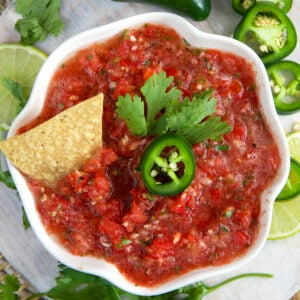 A chip is placed in a bowl full of salsa.