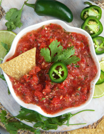 A tortilla chip, jalapeno slice and cilantro leaf are placed on top of salsa.