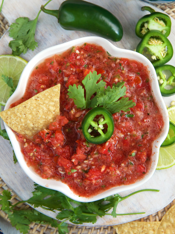 A tortilla chip, jalapeno slice and cilantro leaf are placed on top of salsa.