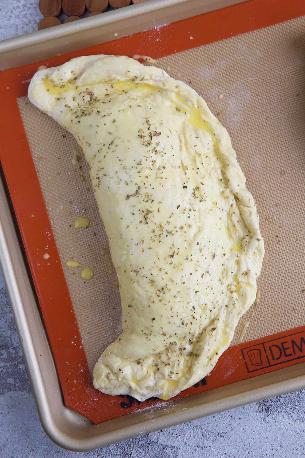 An unbaked calzone is placed on a baking sheet. 