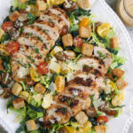 A large white serving platter is topped with chicken caesar salad.