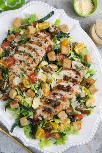 A large white serving platter is topped with chicken caesar salad.