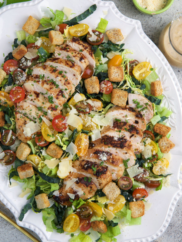 A large white serving platter is topped with chicken caesar salad.