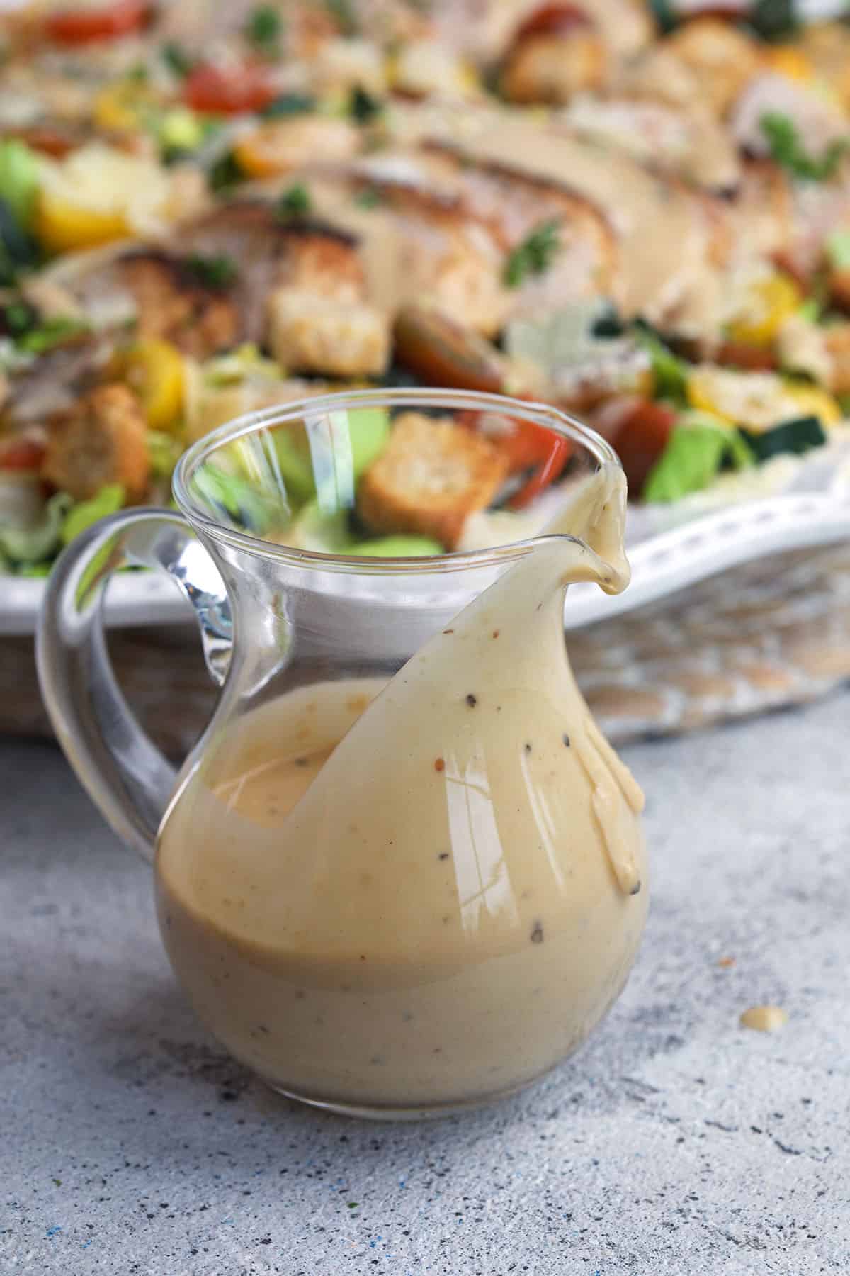 A small glass pitcher is filled with caesar dressing. 