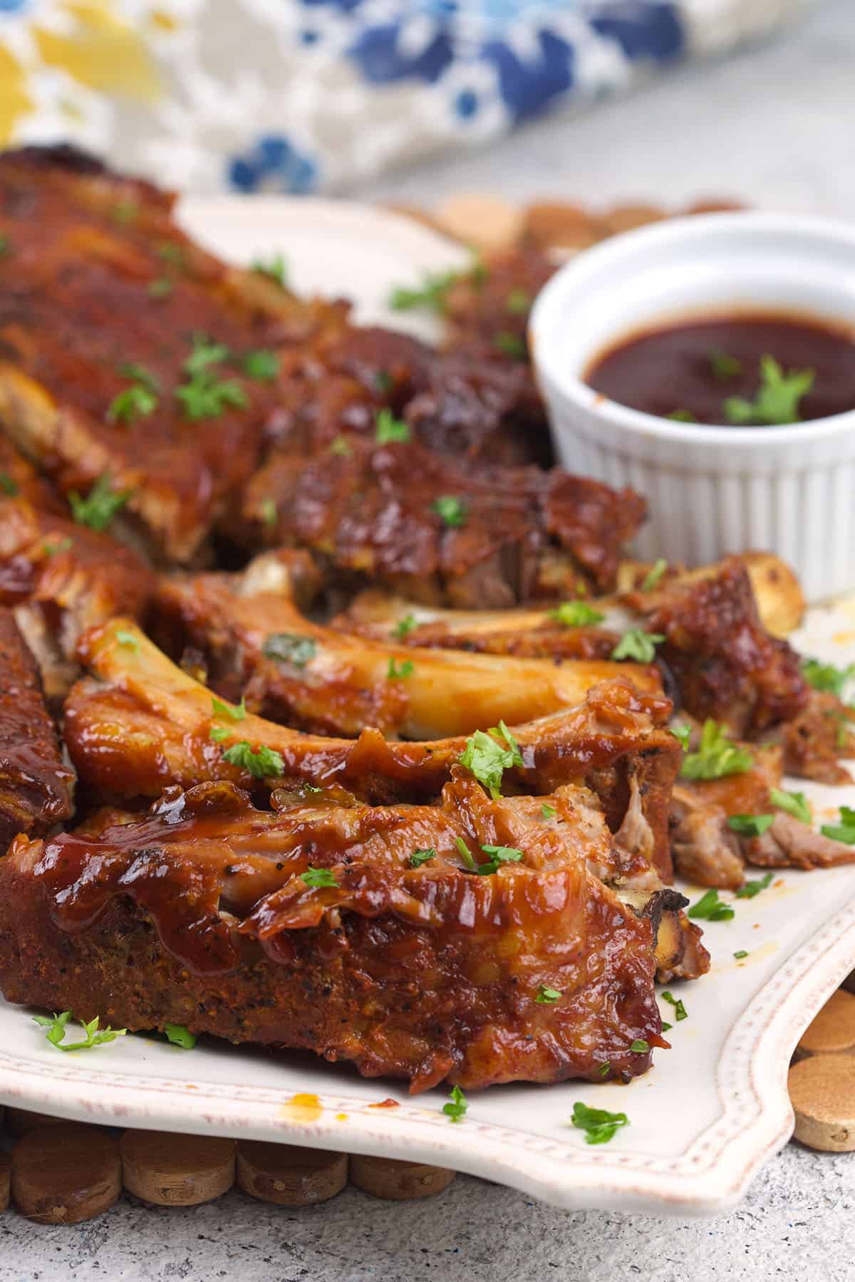 A platter is topped with ribs and a small bowl of barbecue sauce. 