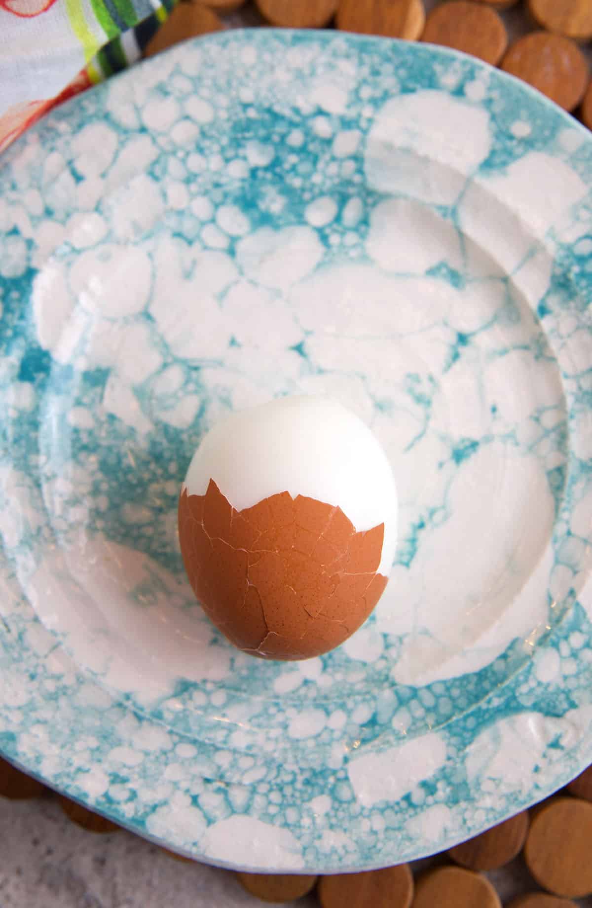 A hard boiled egg is halfway peeled on a blue and white plate. 
