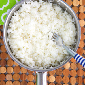 Jasmine rice in a pot is being fluffed with a fork.