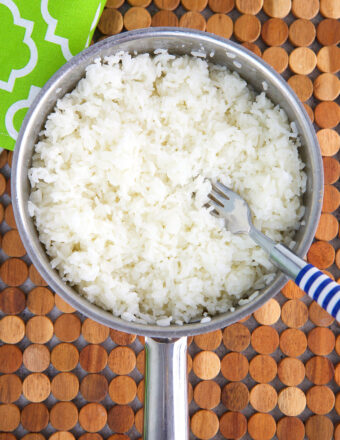 Jasmine rice in a pot is being fluffed with a fork.