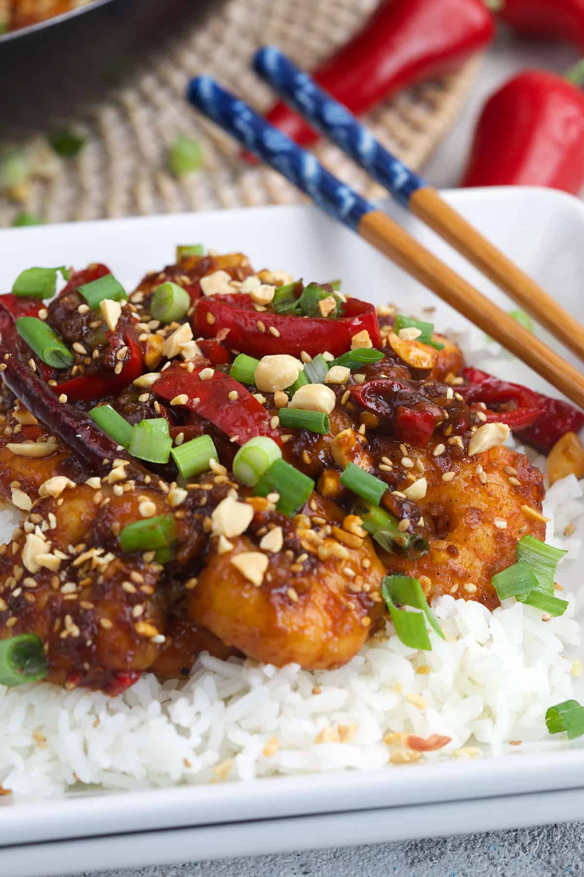A plate of kung pao shrimp is topped with chopsticks. 
