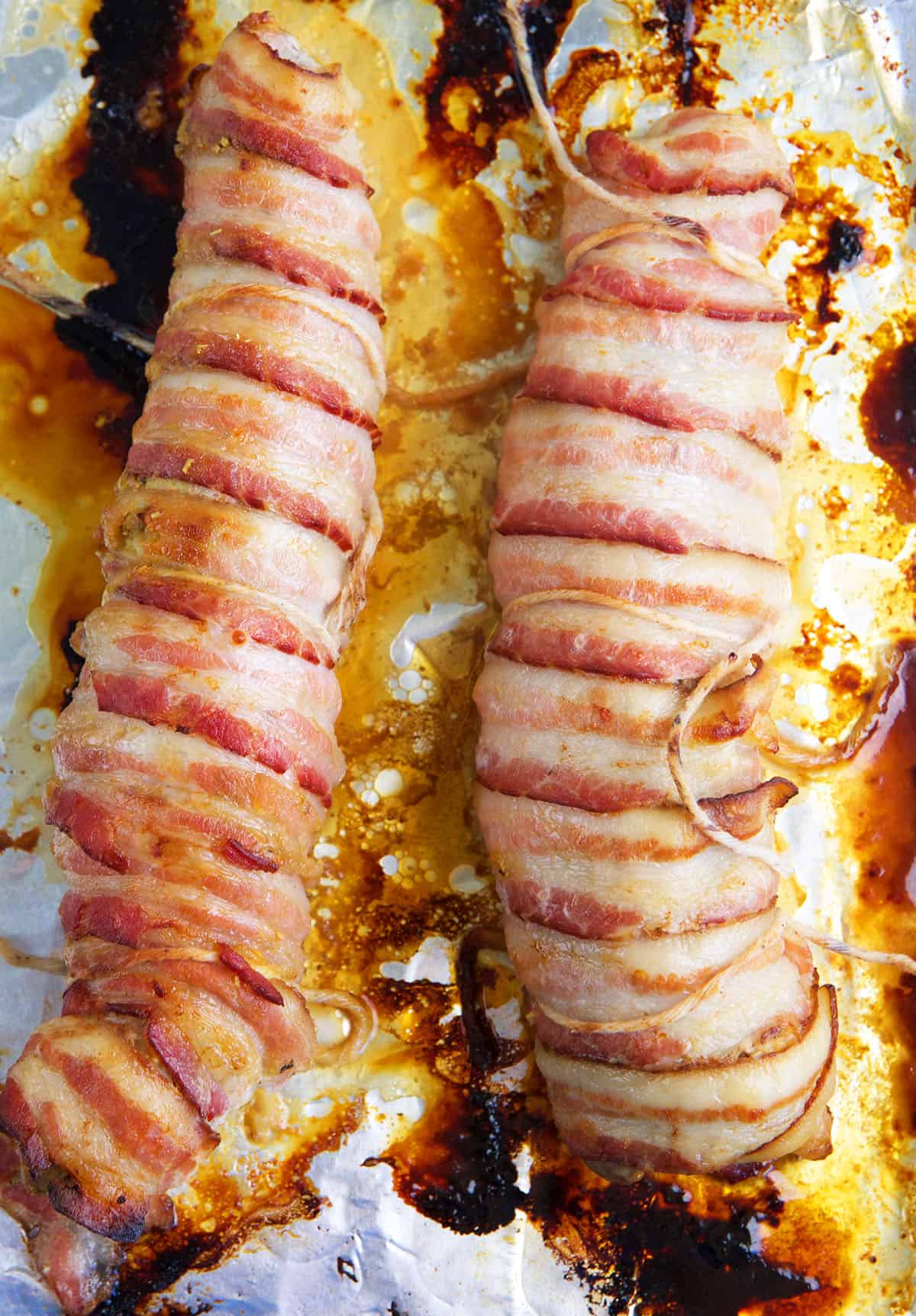 Two bacon wrapped tenderloins are on a foil lined baking sheet. 