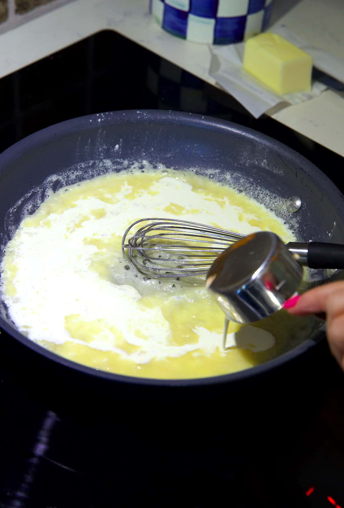 Milk is being whisked into a pan. 