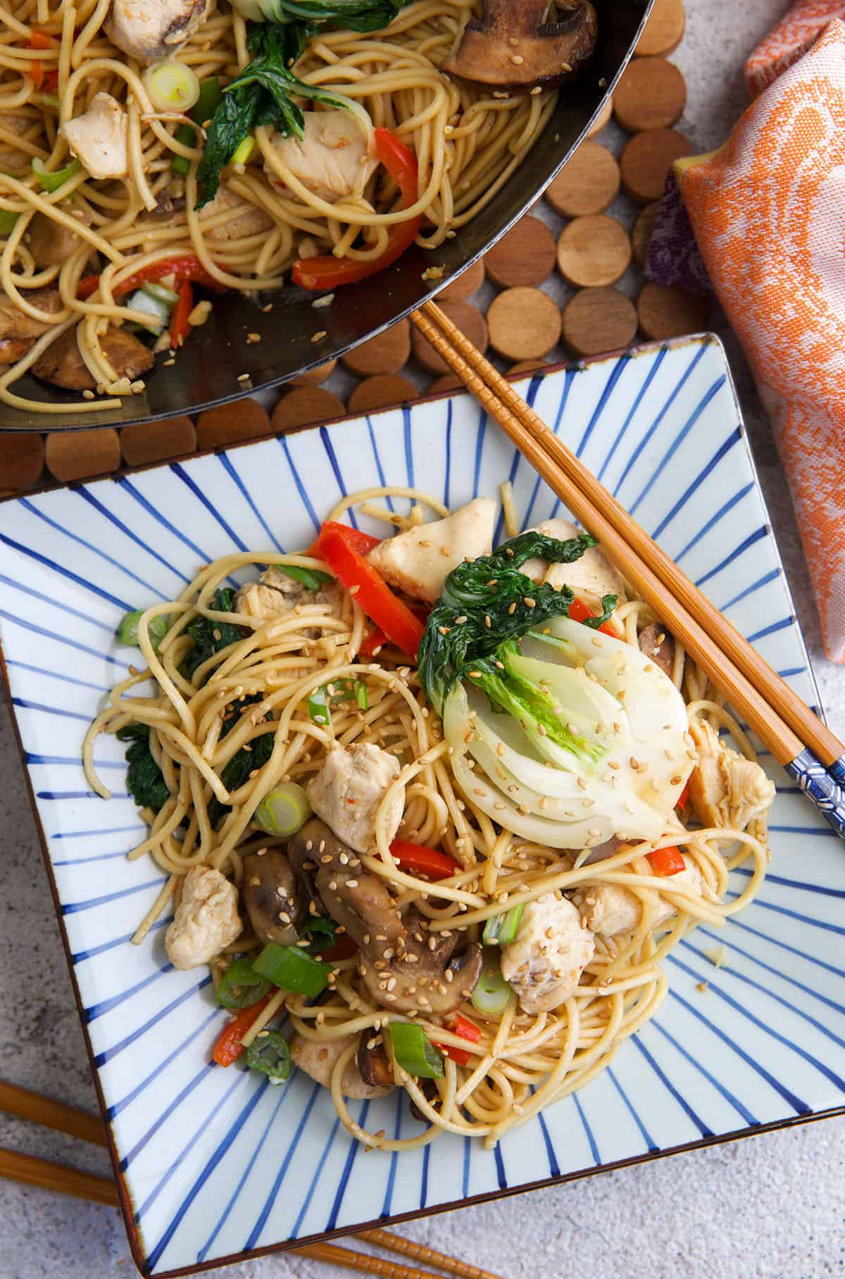 A pair of chopsticks are placed on a plate next to a serving of chow mein. 