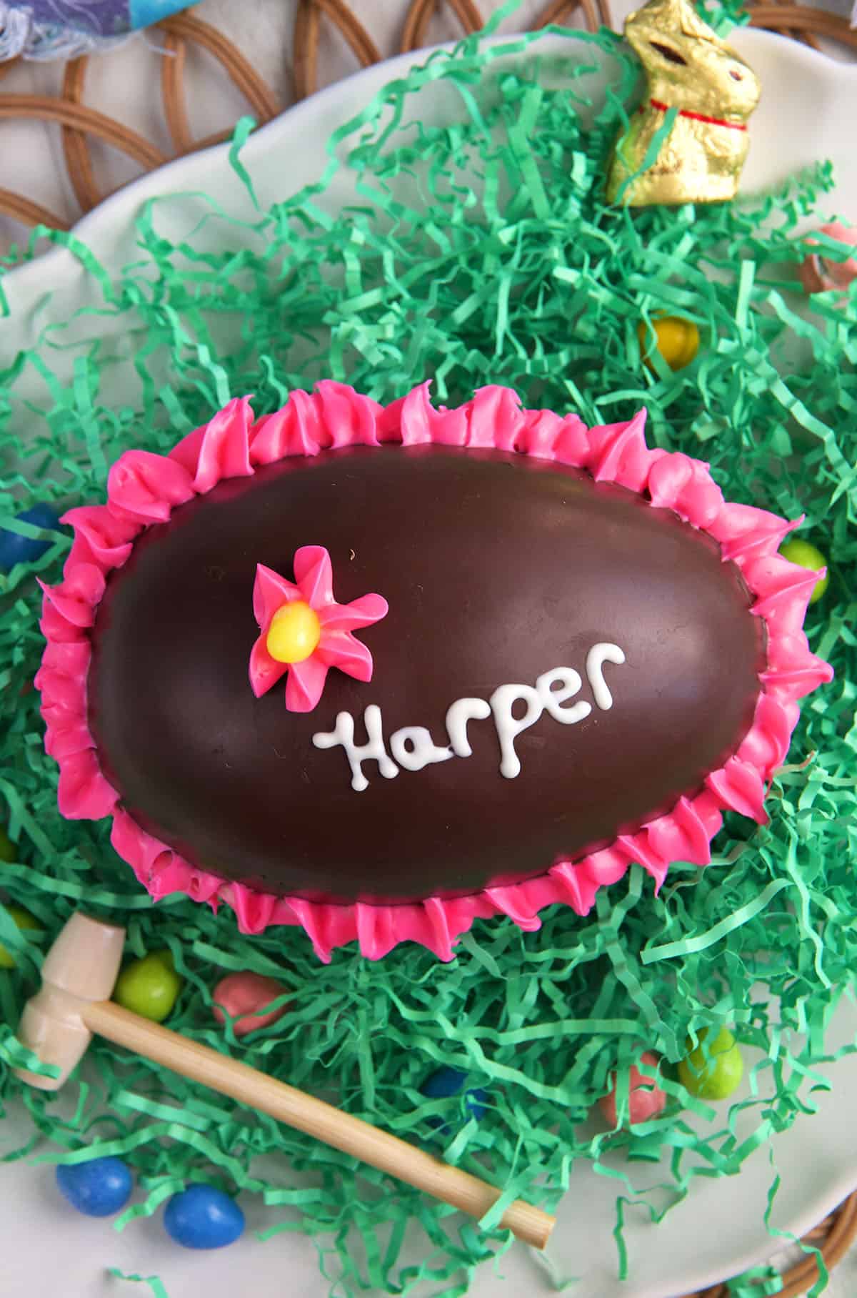 A decorated chocolate easter egg is placed on a bed of green Easter grass. 