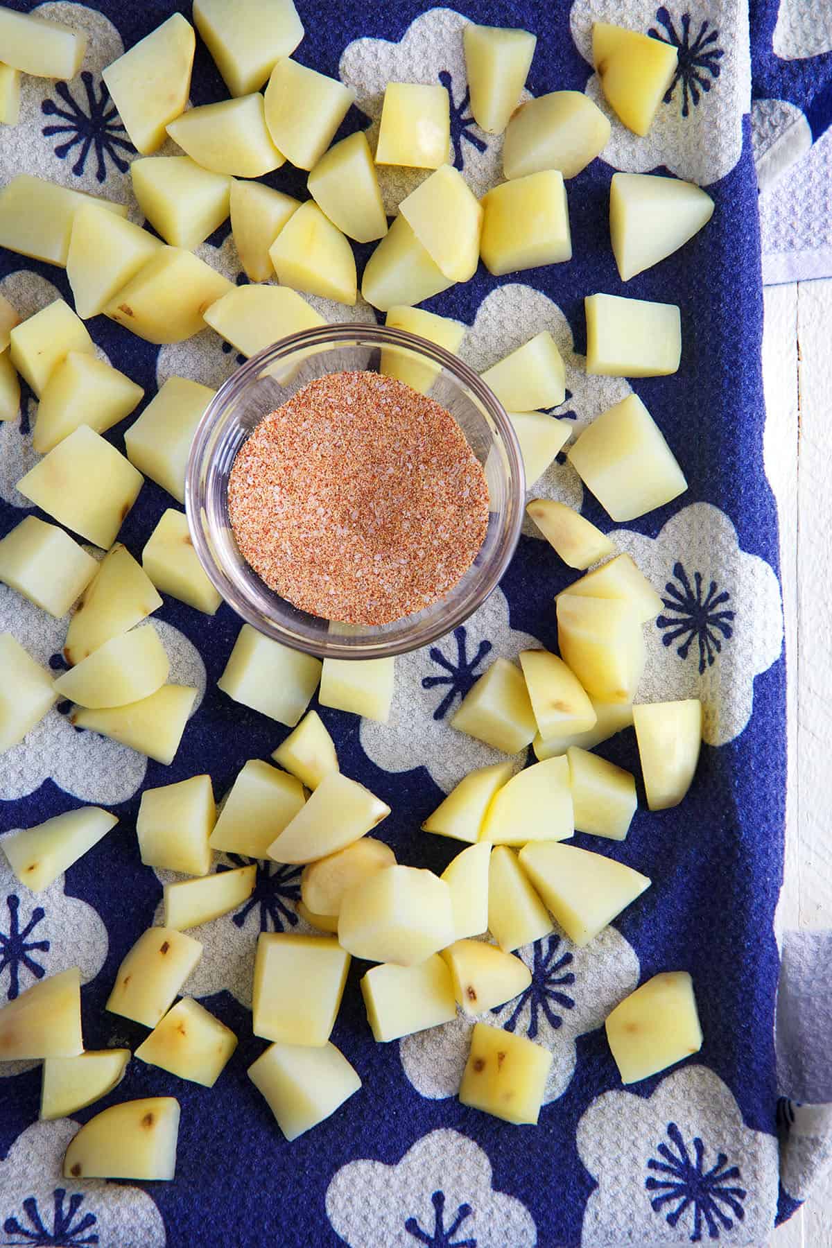 Cubed potatoes are placed next to a small bowl of seasoning. 