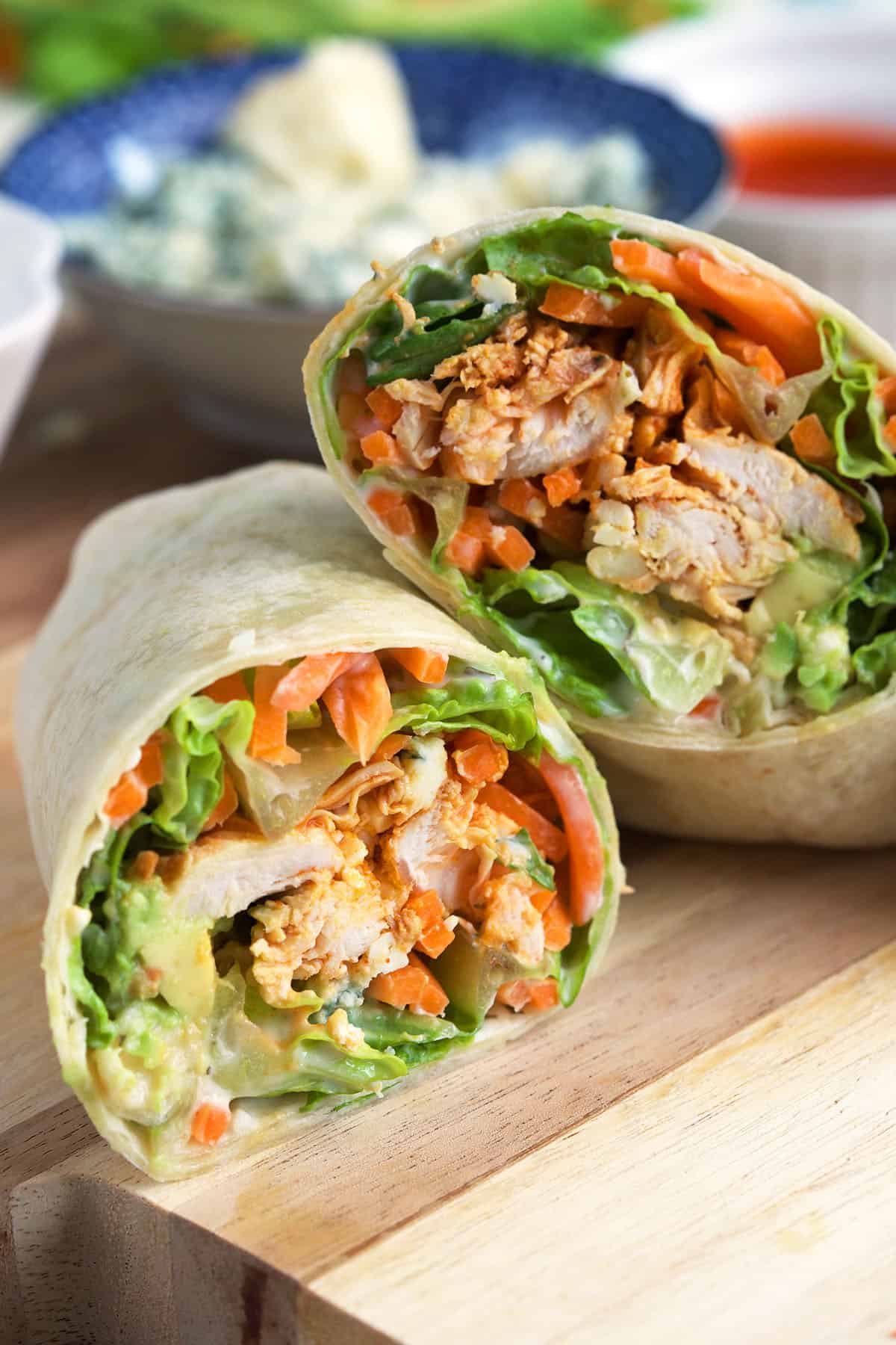 Two halves of a buffalo chicken wrap are placed on a wooden surface. 