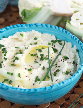 A bowl of mashed potatoes is garnished with chives.