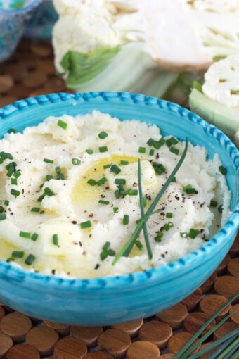 A bowl of mashed potatoes is garnished with chives.