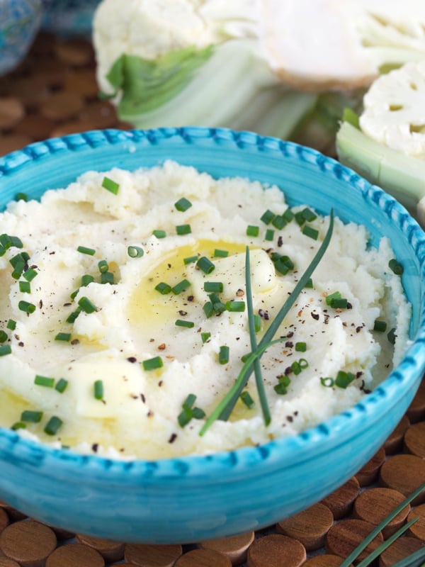 A bowl of mashed potatoes is garnished with chives.
