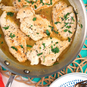 Several chicken breasts are in a skillet with pan sauce.