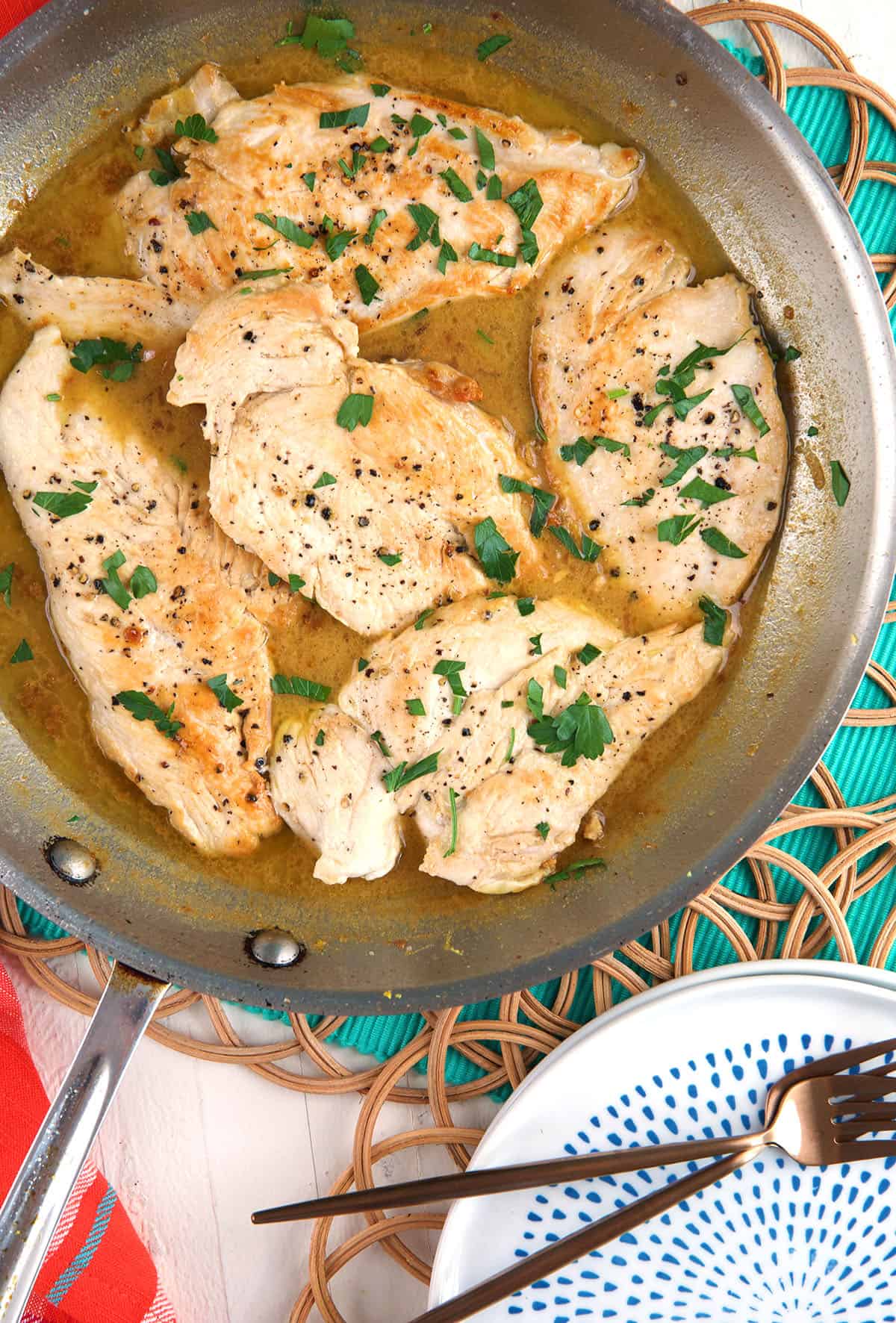Several chicken breasts are in a skillet with pan sauce. 