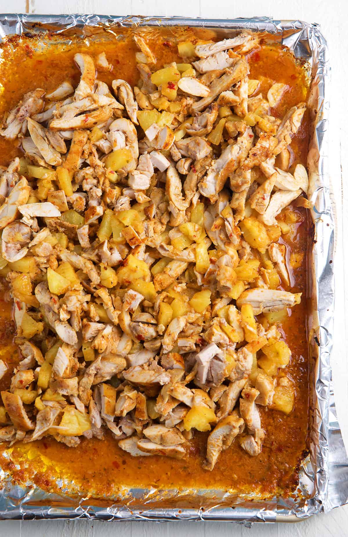 A sheet pan is topped with chopped chicken and pineapples. 